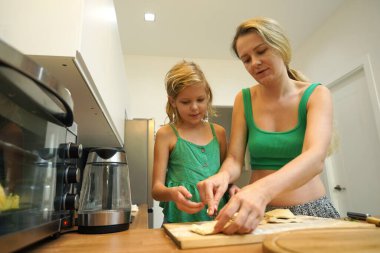 Bir anne ve kızı sıcacık bir mutfakta mutlu bir şekilde yemek pişiriyor.