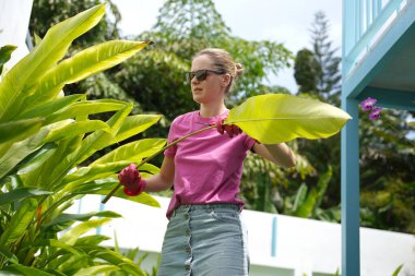 Genç bir kadın güzel bahçesini süslüyor canlı yeşilliğini ve açık hava aktivitelerine olan aşkını sergiliyor.