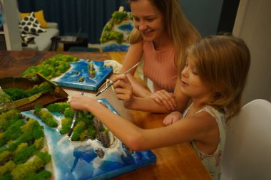 Genç bir anne ve kızı birlikte canlı doğal manzaralar yaratıyor. 