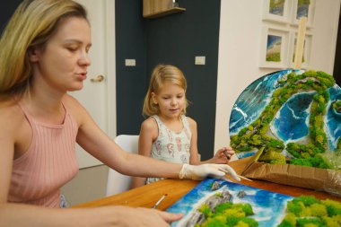 Genç bir anne ve kızı birlikte canlı doğal manzaralar yaratıyor. 