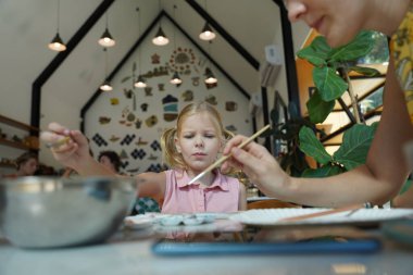 Genç bir anne ve kızı evde sanatsal bir seansın keyfini çıkarıyorlar. Renkli sanatlarıyla meşgul ve bağ kuruyorlar.
