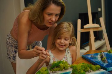 Genç bir anne ve kızı birlikte canlı doğal manzaralar yaratıyor. 