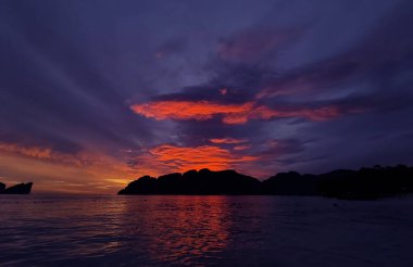 Çarpıcı bir günbatımı, kıyı şeridi manzarası boyunca sakin bir okyanusun üzerinde canlı renkler bırakıyor.