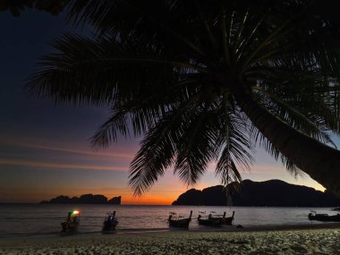 Çarpıcı bir günbatımı, kıyı şeridi manzarası boyunca sakin bir okyanusun üzerinde canlı renkler bırakıyor.