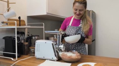 Çağdaş bir mutfakta et öğüten genç bir kadın kıyma makinesi kullanıyor.