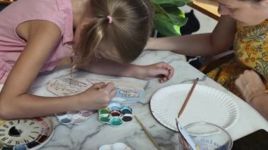 Genç bir anne ve kızı evde sanatsal bir seansın keyfini çıkarıyorlar. Renkli sanatlarıyla meşgul ve bağ kuruyorlar.