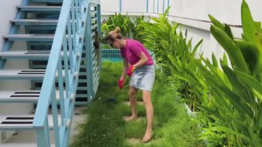 Evinin arka bahçesindeki çimenleri tırmıklayan genç bir kadın. 