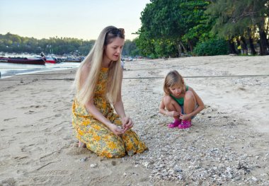 Kumsalda deniz kabuğu toplarken bir anne ve kızı