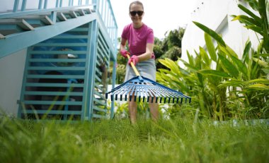 Evinin arka bahçesindeki çimenleri tırmıklayan genç bir kadın. 