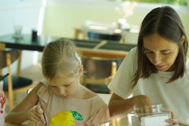 Sanat öğretmeni atölyede iki kıza termo mozaik montajı öğretiyor. 