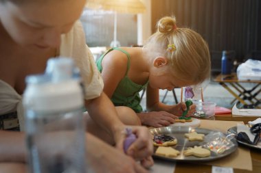 Genç anne ve kızı cadılar bayramı kurabiyelerini geniş bir modern atölyede boyuyorlar.