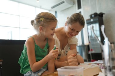 Young mother and her daughter paint Halloween cookies in a spacious modern workshop clipart