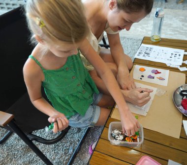 Young mother and her daughter paint Halloween cookies in a spacious modern workshop clipart