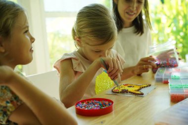 Sanat öğretmeni atölyede iki kıza termo mozaik montajı öğretiyor. 