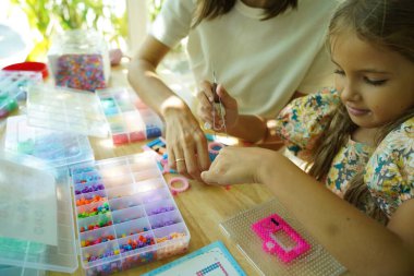 Sanat öğretmeni atölyede iki kıza termo mozaik montajı öğretiyor. 