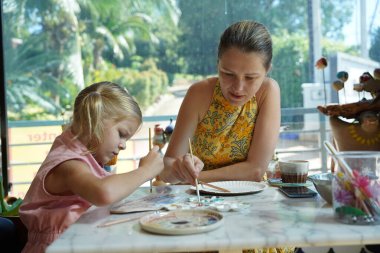Genç bir anne ve kızı evde sanatsal bir seansın keyfini çıkarıyorlar. Renkli sanatlarıyla meşgul ve bağ kuruyorlar.