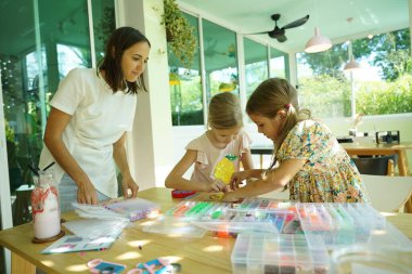 Sanat öğretmeni atölyede iki kıza termo mozaik montajı öğretiyor. 