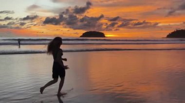 Gün batımında sakin sahil sahnesinde koşan ve yürüyen bir kadın. 