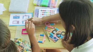 Sanat öğretmeni atölyede iki kıza termo mozaik montajı öğretiyor. 