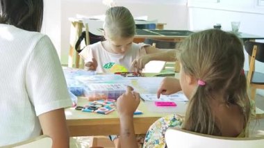 Sanat öğretmeni atölyede iki kıza termo mozaik montajı öğretiyor. 