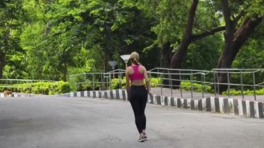 Bir kadın, yemyeşil ve çarpıcı kıyı manzaralarıyla çevrili güzel, dolambaçlı bir yolda koşuyor.