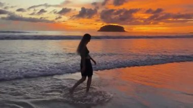 Gün batımında sakin sahil sahnesinde koşan ve yürüyen bir kadın. 
