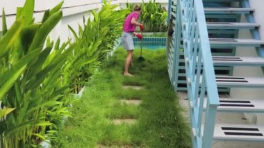 Evinin arka bahçesindeki çimenleri tırmıklayan genç bir kadın. 