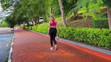 Bir kadın, yemyeşil ve çarpıcı kıyı manzaralarıyla çevrili güzel, dolambaçlı bir yolda koşuyor.