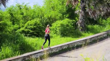 Bir kadın, yemyeşil ve çarpıcı kıyı manzaralarıyla çevrili güzel, dolambaçlı bir yolda koşuyor.