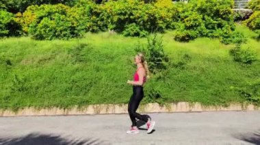 Bir kadın, yemyeşil ve çarpıcı kıyı manzaralarıyla çevrili güzel, dolambaçlı bir yolda koşuyor.