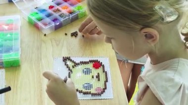 Sanat öğretmeni atölyede iki kıza termo mozaik montajı öğretiyor. 