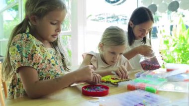 Sanat öğretmeni atölyede iki kıza termo mozaik montajı öğretiyor. 