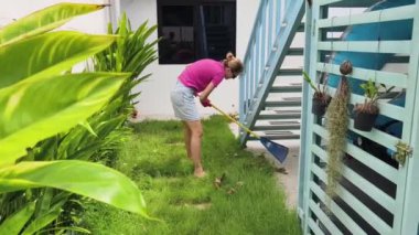 Evinin arka bahçesindeki çimenleri tırmıklayan genç bir kadın. 