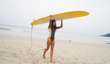 Dar dalış kıyafeti giyen güzel genç bir kadın güzel bir sahilde sörf tahtasına çıkacak..