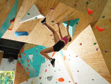 Güçlü bir dişi tırmanıcı renkli saplı yapay bir duvara tırmanır..