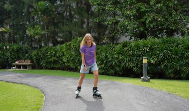 Bir kadın, güzel bir park ortamında uzanan manzaralı bir yolda paten kaymaktan zevk alıyor..