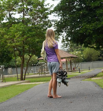 Bir kadın, güzel bir park ortamında uzanan manzaralı bir yolda paten kaymaktan zevk alıyor..