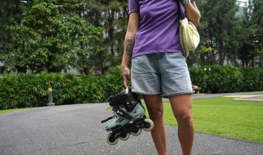 Bir kadın, güzel bir park ortamında uzanan manzaralı bir yolda paten kaymaktan zevk alıyor..