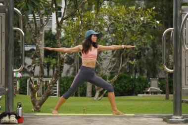 Genç bir kadın güzel bir şehir parkında yoga minderi yapıyor.