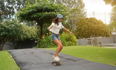 Güzel genç bir kadın ustalıkla kaykayla parktan geçiyor.