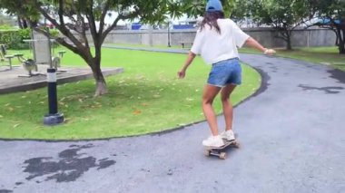 Güzel genç bir kadın ustalıkla kaykayla parktan geçiyor.