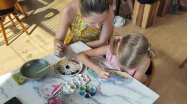 Genç bir anne ve kızı evde sanatsal bir seansın keyfini çıkarıyorlar. Renkli sanatlarıyla meşgul ve bağ kuruyorlar.