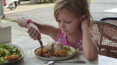 Neşeli küçük bir kız kafede kızarmış tavuk ve taze salata yiyor.