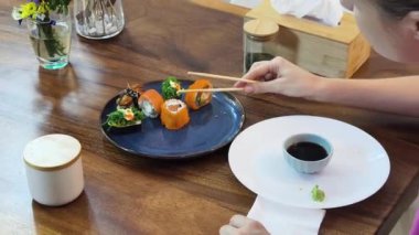 Sıcak bir yemek masasında oturmuş lezzetli suşiden zevk alan genç bir kadın. 