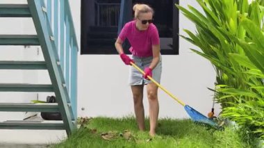 Evinin arka bahçesindeki çimenleri tırmıklayan genç bir kadın. 