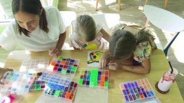 Sanat öğretmeni atölyede iki kıza termo mozaik montajı öğretiyor. 
