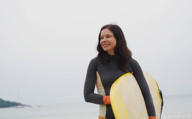 Dar dalış kıyafeti giyen güzel genç bir kadın güzel bir sahilde sörf tahtasına çıkacak..