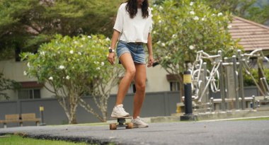 Güzel genç bir kadın ustalıkla kaykayla parktan geçiyor.