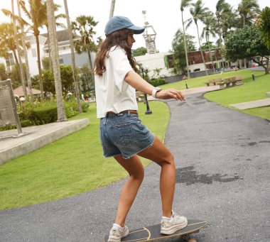 Güzel genç bir kadın ustalıkla kaykayla parktan geçiyor.