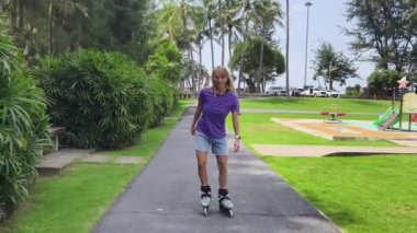 Bir kadın, güzel bir park ortamında uzanan manzaralı bir yolda paten kaymaktan zevk alıyor..